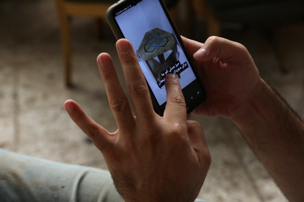 Two hands hold a phone depicting a branded table for sale and text.