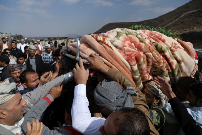 A crowd of men reach up to support a coffin draped in a blanket.