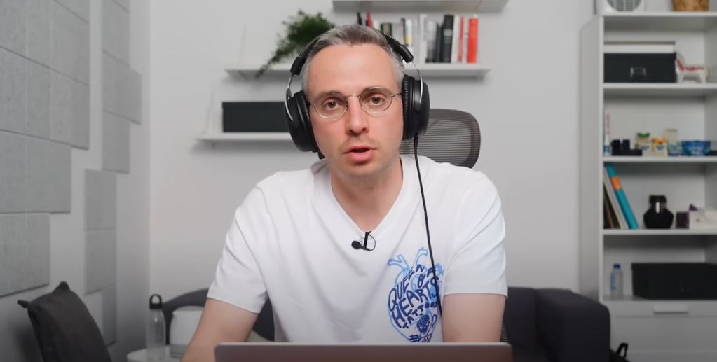 A man wearing headphones talks in front of a laptop.