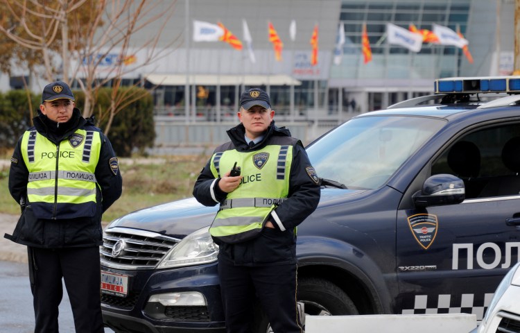 Two police officers stand in front of a police car.