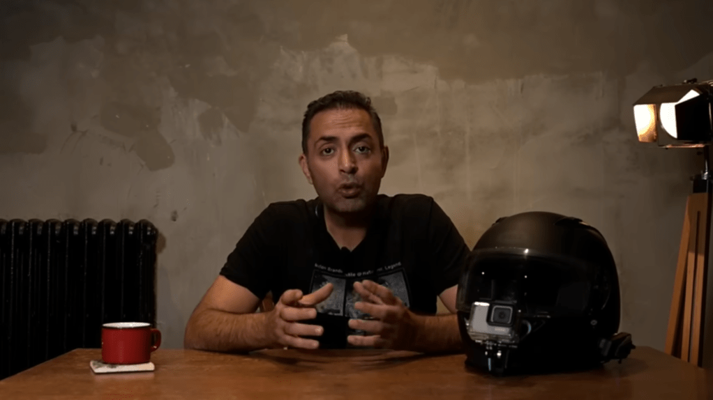 A man speaks to the camera at a desk.