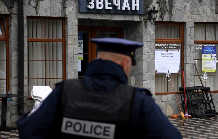 The back of a police officer in front of a stone building.