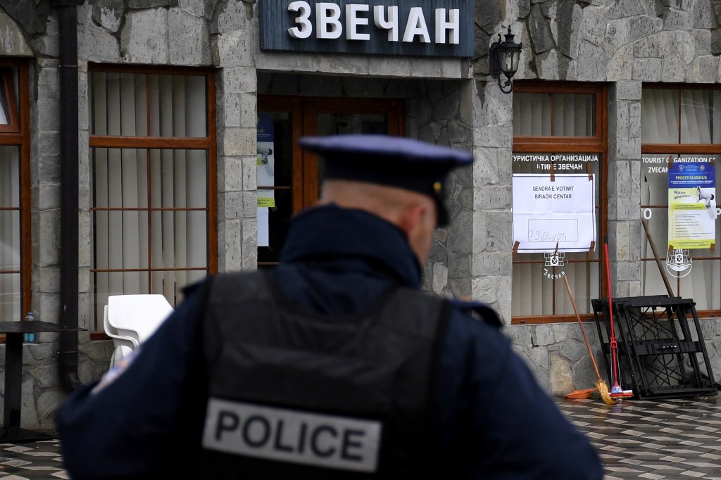 The back of a police officer in front of a stone building.