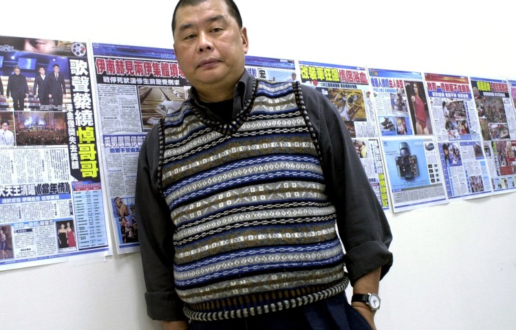 A man stands before a wall of newspapers.