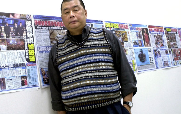 A man stands before a wall of newspapers.