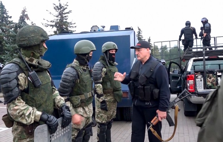 A man carrying a rifle talks to three men in green military gear.