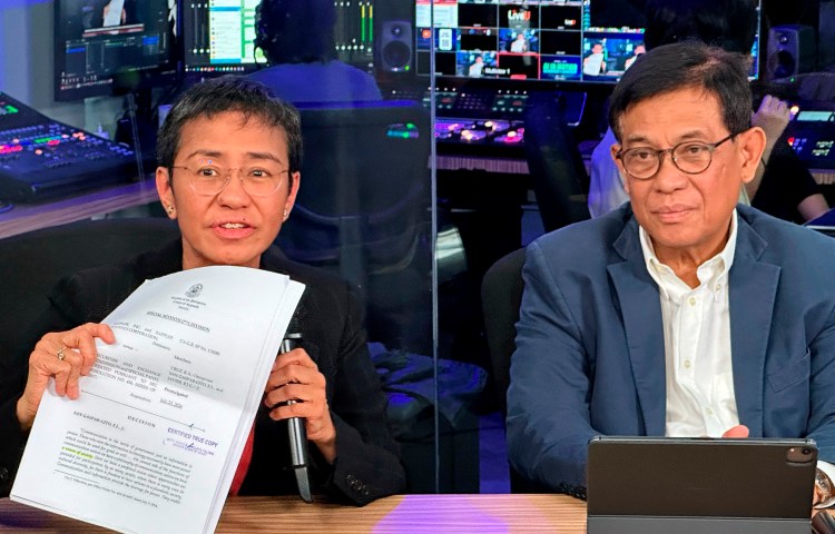 Maria Ressa, Nobel laureate and co-founder of Rappler, displays documents showing the court's decision to allow the news site to keep operating, seated by her lawyer Francis Lim, at a news conference in Rappler's office in the Philippine capital Manila on August 9.