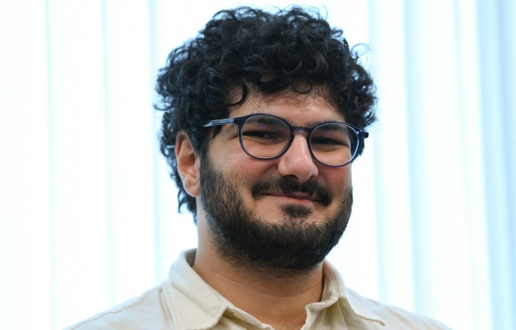 A man with curly hair and glasses smiles at the camera.