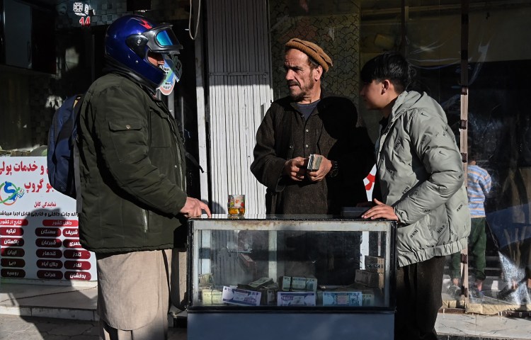 An Afghan money changer holding banknotes speaks with a customer at a currency exchange market in Kabul in January, following the decline in the afghani currency against US dollars.