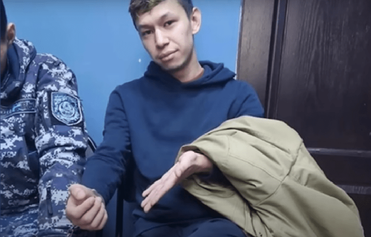 Temirlan Yensebek, founder of the Kazakh satirical outlet Qaznews24 gestures to his handcuff while seated in a police station in the capital Almaty on January 17.