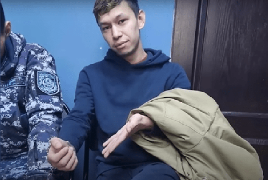 Temirlan Yensebek, founder of the Kazakh satirical outlet Qaznews24 gestures to his handcuff while seated in a police station in the capital Almaty on January 17.